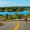 Guest cycling down road, large lake or river in background.