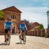 Two guests cycling down brick road, small church in background.