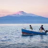 Two locals on boat during sunset, large mountain in distance.