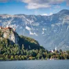 Wide shot of Bled Castle, town, lake below, mountain behind.