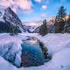 Wide shot of snowy valley, mountains, trees around.