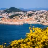 Wide shot of Dubrovnik coastline, blue ocean, white and tan houses.