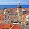 Wide shot of Dubrovnik coastline, blue ocean, white and tan houses.