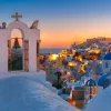 Sunset shot of Santorini, city lit up, church bell in foreground.