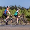 Two guests on e-bikes riding past vineyard.