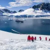 Hikers trekking up a snowy hill in Antarctica with a cruise ship anchored in the background