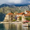 Shot of Croatian houses on coast, boats, mountain in distance.