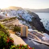 Wide shot of Santorini cliffside, white houses, ocean, sunset.