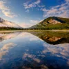 Wide shot of reflective lake, mountains during sunset.