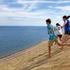 Group of young guests running down sand dune towards ocean.