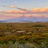 Purple and orange sunset with scenic green field and rocky mountains