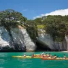 Guests kayaking away from beach, white stone cliff behind them. 