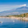 Wide shot of Mount Etna, small boats in water in foreground.