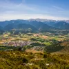 Bird's eye shot of mountainous valley, town, golden fields below.