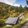 Two hikers walking on a trail past small wooden huts.