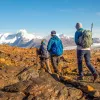 Three guests walking over orange rocks, snowy peaks in distance.