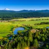 Wide shot of green pasture, large house in foreground, mountains in background.
