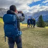 One guest taking photo of other three, mountains behind them.