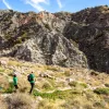 Group of three hiking in desert, craggy hill in background.