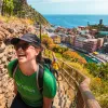 Two guests hiking up rocky trail, colorful coastal town in background.