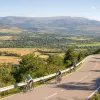 Group of 3 people riding bikes on an asphalt road, with valleys of trees in the distance