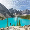 Man standing on a boulder, looking out to a blue lake and tall trees