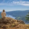 Woman sitting on a large boulder on top of a hill, looking down at the water