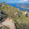 Group of people hiking on a trail along a cliff, with the ocean and an island in the distance