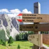 Wooden sign with red and white arrows, with tall rocky mountains in the background
