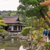 Three people walking on a small path on the right towards a Japanese-style building in the forest