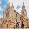 Man and woman biking in front of a stone cathedral
