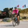 Woman in pink, biking in front of a green tank with flags waiving in the background