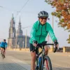 Woman wearing a green jacket, smiling while riding a bike and a cathedral in the background