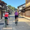 Two men biking on a stone road in the middle of a Japanese town