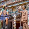 Woman riding a bike in front of a large temple, with a man smiling and waving at her