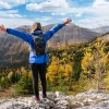Woman wearing a blue jacket on top of a cliff with her arms wide open