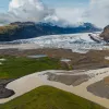 Valley with a brown river, in front of a large lake with ice caps behind it