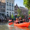 Two women paddling in a red kayak with a European town in the background