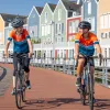 Man and woman biking on a wooden bike path with rows of colorful houses behind them
