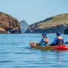 Two people paddling on an orange kayak in the middle of a lake