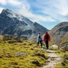 Man and woman ascending a rocky, dirt trail with large mountains ahead