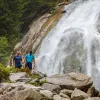 Two men hiking on a rocky trail next to a waterfall