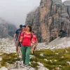 Three women and one man hiking on a grassy trail with fog-covered mountains in the background
