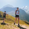 Two women smiling, while hiking on a dirt trail on top of a mountain