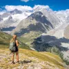 Woman wearing a backpack, looking out to a large valley of mountains and trees