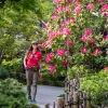 Woman smiling while walking through an outdoor garden full of plants and pink flowers
