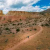 Top view of a man in blue ascending a dirt trail towards a mountain