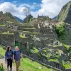 Man and woman smiling while walking on a stone path, with Machu Picchu in the background