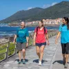 Three women walking on a stone path next to the ocean side