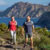 Man and woman smiling while walking on a dirt and stone path and the ocean in the background